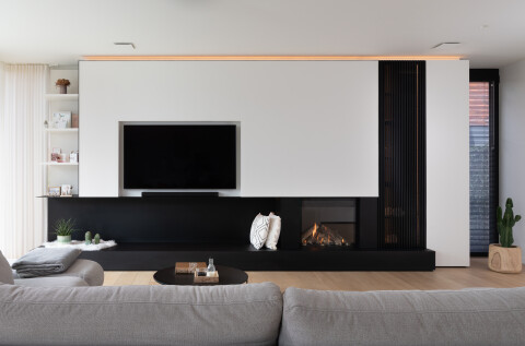 Moderne woonkamer met een strak tv-meubel en ingebouwde haard, gekenmerkt door minimalistische lijnen en een rustige uitstraling.